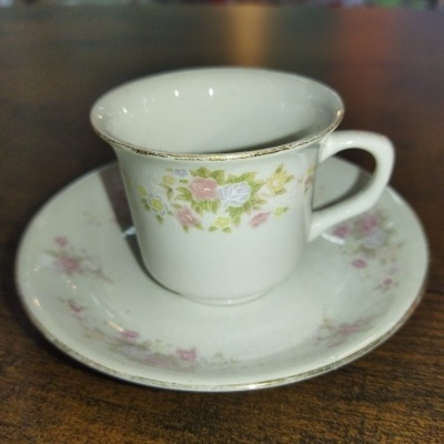 Chávena e pires de porcelana branca com flores e bordas douradas em mesa de madeira.