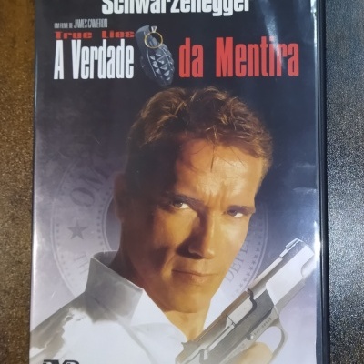 Capa de DVD do filme A Verdade da Mentira com Schwarzenegger segurando arma