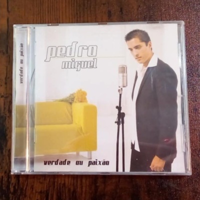 Capa de CD de Pedro Miquel com texto e imagem do cantor ao lado de um microfone e um sofá amarelo