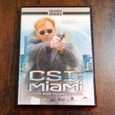Capa de DVD da série CSI Miami com homem loiro de óculos escuros e arma