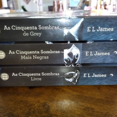 Três livros da coleção As Cinquenta Sombras de Grey de E L James empilhados.
