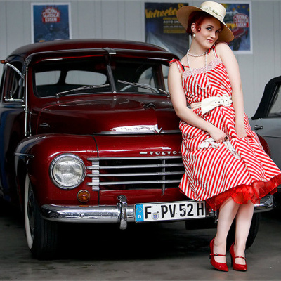 Mulher com vestido listrado vermelho e branco sentada em carro clássico Volvo vermelho com matrícula alemã