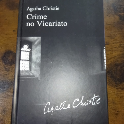 Livro capa dura preta com texto e imagem de janela em cinza sobre madeira.