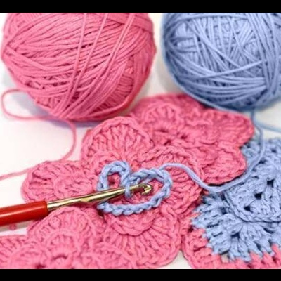 Linhas de lã rosa e azul com croché e agulha vermelha.