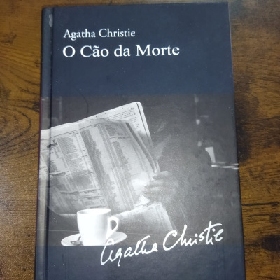 Livro O Cão da Morte de Agatha Christie com capa preta e imagem de xícara de café e jornal