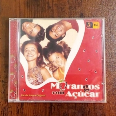 Capa de CD Morangos com Açúcar com quatro jovens sorridentes, fundo vermelho com sementes de morango
