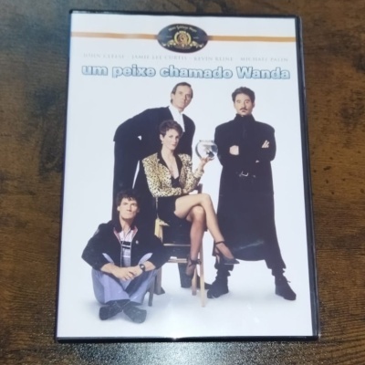 Capa de DVD do filme 'um peixe chamado Wanda' com quatro pessoas, mulher segurando aquário, fundo branco