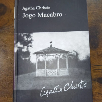 Livro Jogo Macabro de Agatha Christie com capa preta e foto a preto e branco de quiosque com corvo