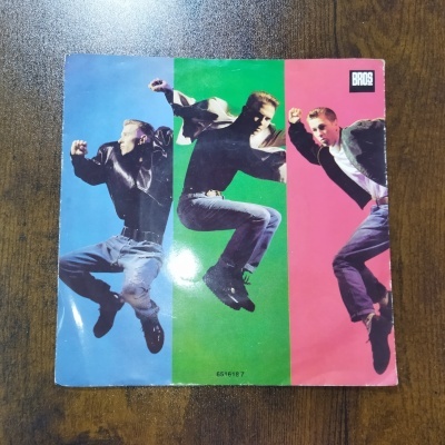 Capa de disco em papel brilhante com três imagens de homens a saltar, fundo colorido e texto BROS