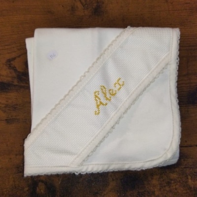 Manta branca com bordado 'Alex' dobrada numa mesa de madeira