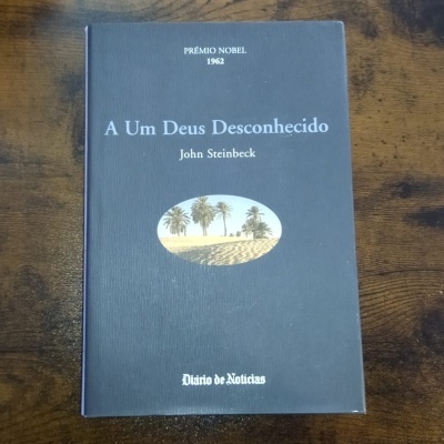 Capa de livro azul com título 'A Um Deus Desconhecido' e autor John Steinbeck