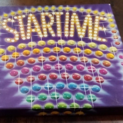 Caixa de jogo de tabuleiro STARTIME colorida com bolinhas sobre mesa de madeira