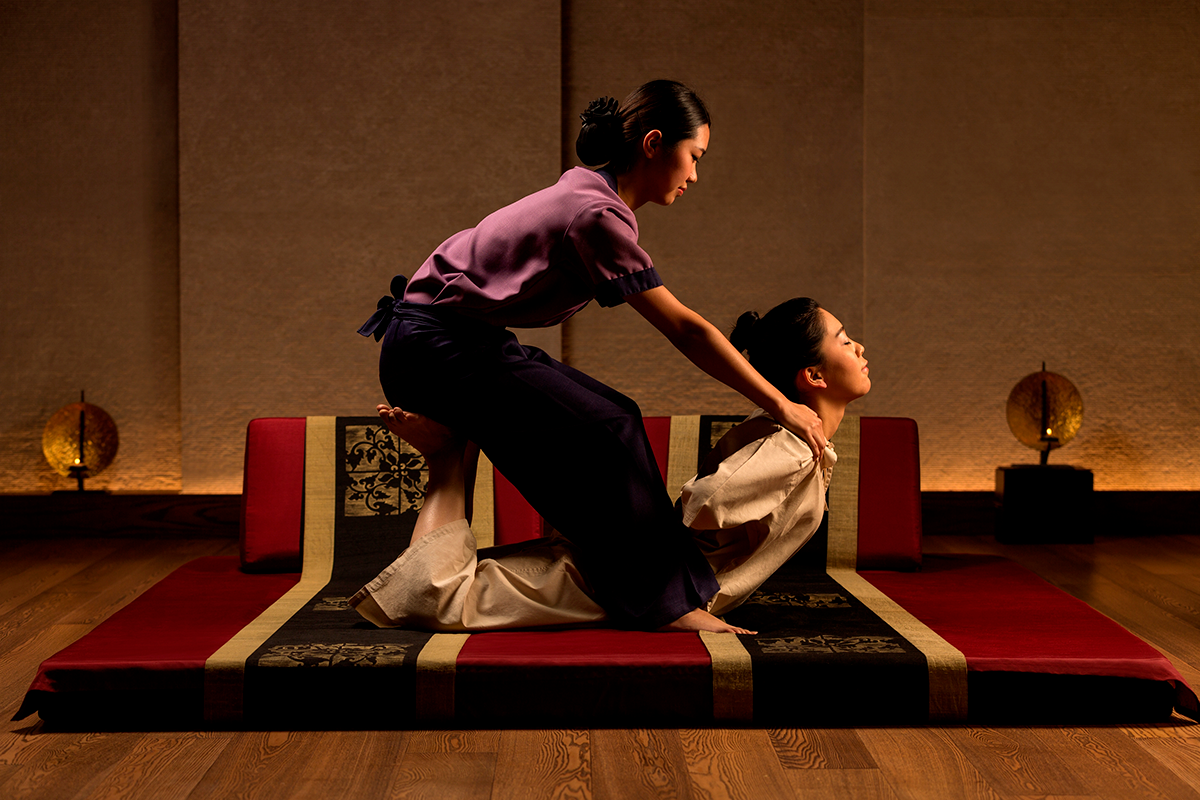 Massagem - Essência Tailandesa 60/90min Duas mulheres em tatami decorativo com padrões florais e geométricos