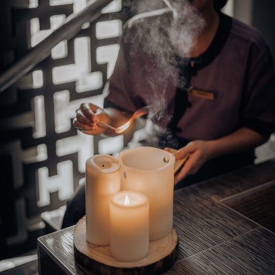 Três velas brancas acesas sobre base de madeira e pessoa a acender uma vela com fósforo
