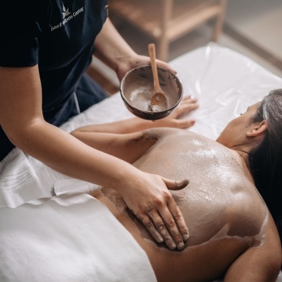 Pessoa a receber massagem nas costas com loção branca, terapeuta com uniforme preto e texto Relax & wellness Center