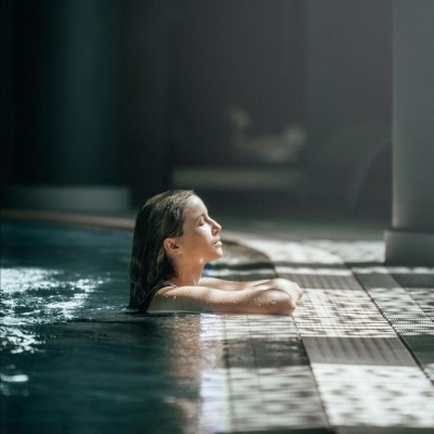 Mulher na piscina encostada na borda com azulejos brancos e cinzentos