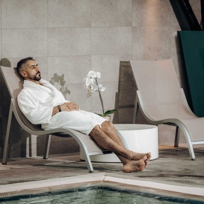 Homem de roupão branco numa espreguiçadeira junto a piscina interior