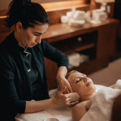 Massagem facial profissional numa mulher deitada numa sala de estética acolhedora.