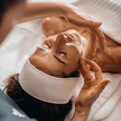 Pessoa a receber massagem facial com bandana branca e toalha branca.