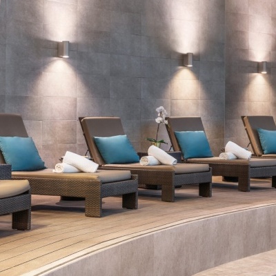 Espreguiçadeiras rattan com almofadas e toalhas numa área interior iluminada.