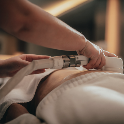 Tratamento corporal com aparelho branco na zona abdominal de pessoa deitada coberta por toalha