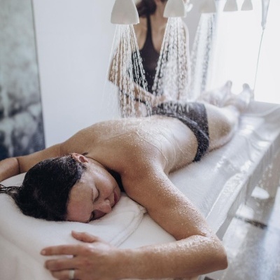 Pessoa deitada a receber tratamento de jatos de água em cama branca com toalha