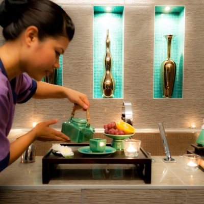 Mulher servindo chá verde num serviço de chá em ambiente moderno com decoração dourada e frutas