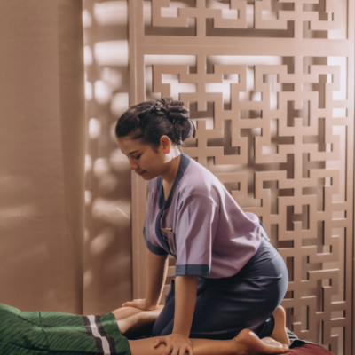 Masseuse a fazer massagem numa pessoa deitada numa cama com lençóis verdes e vermelhos