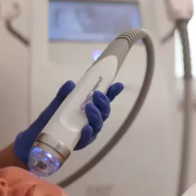 Dispositivo estético branco com luz azul em uso no rosto de mulher numa clínica