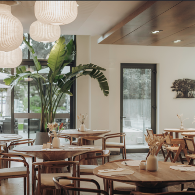 Restaurante moderno com mesas e cadeiras de madeira, plantas e luminárias brancas