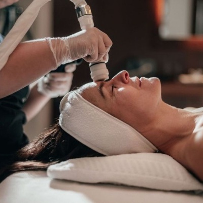 Mulher deitada a receber tratamento facial com dispositivo branco e bege