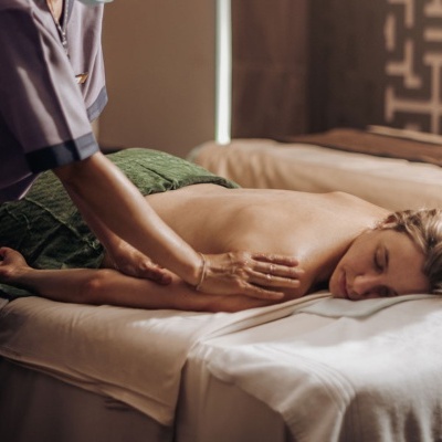 Pessoa a receber massagem numa cama com lençóis brancos em ambiente interior acolhedor