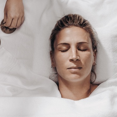 Mulher de olhos fechados deitada numa cama branca com discos redondos de madeira