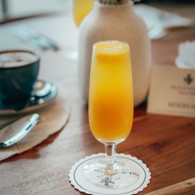 Taça de sumo laranja sobre suporte branco, com caneca azul e vaso ao fundo