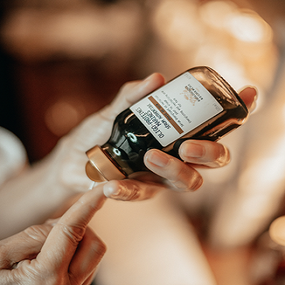 Frasco de vidro castanho com rótulo branco e tampa dourada segurado por mãos