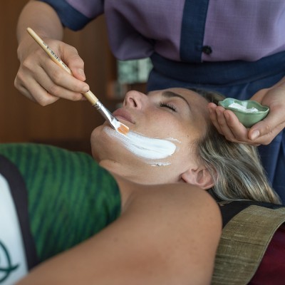 Aplicação de creme facial com pincel num rosto de uma pessoa que está deitada