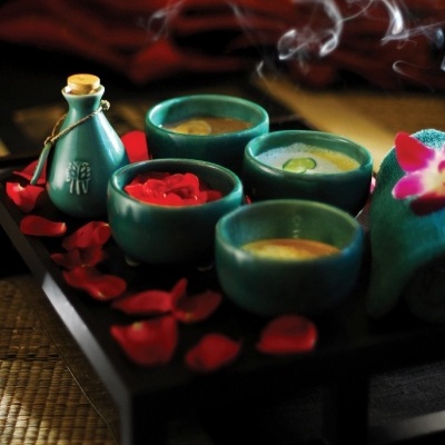 Conjunto cerâmico verde com taças e garrafa numa bandeja preta com pétalas vermelhas e toalha verde com orquídea