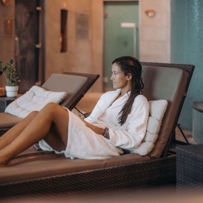 Espreguiçadeira de vime castanho com almofada bege e mulher com robe branco