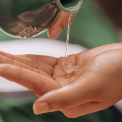 Líquido transparente sendo derramado na mão de um recipiente metálico