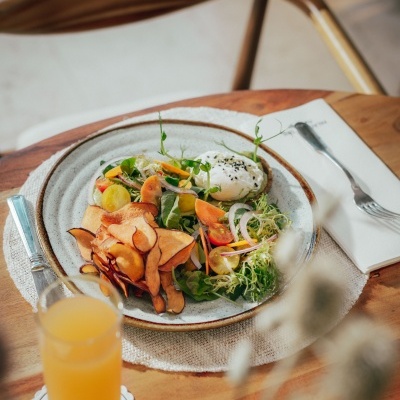 Prato com salada, ovo estrelado e batata-doce frita numa mesa de madeira com sumo de laranja