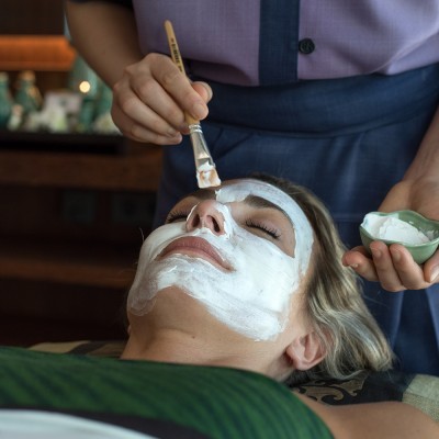 Aplicação de máscara facial branca num rosto feminino com pincel e creme