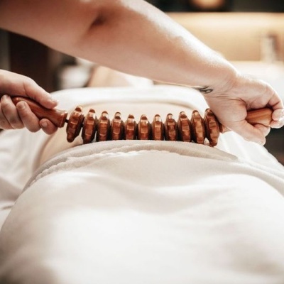 Rolo de madeira para massagem sobre costas cobertas por lençol branco