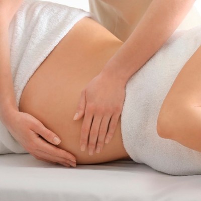 Massagem abdominal com mãos sobre a barriga de uma pessoa envolta em toalha branca.