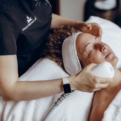Tratamento facial a laser em mulher deitada com toalha branca e faixa na cabeça
