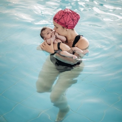 Mulher com touca rosa segura bebé na piscina de água azul
