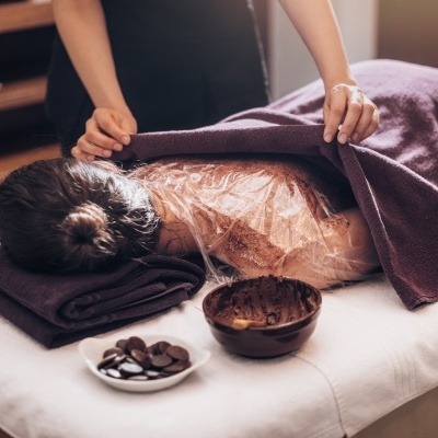Pessoa recebendo tratamento corporal com envoltório plástico e creme num spa.