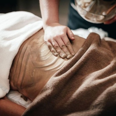 Massagem corporal com aplicação de óleo na barriga com mantas castanha e branca