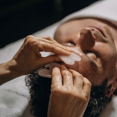 Homem a receber massagem facial com pedra de Gua Sha branca