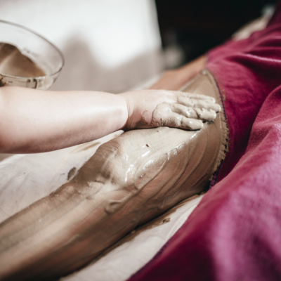 Pessoa aplicando máscara de lama nas pernas de outra em ambiente de spa