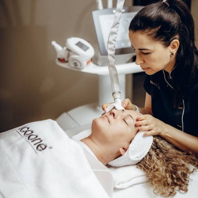 Tratamento facial com aparelho estético em cliente deitada coberta por toalha branca D-Goone